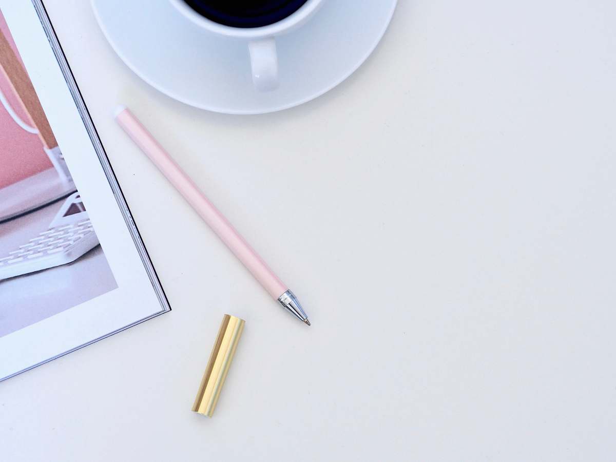 australia pink pen beside white ceramic teacup on white surface minimal